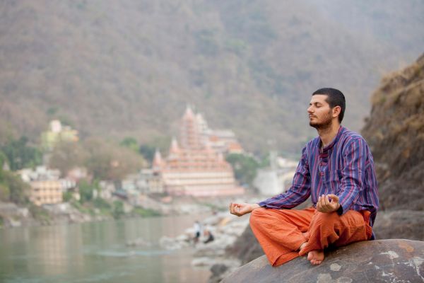 Man meditating by the riverside in yoga pose